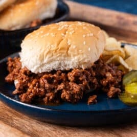 homemade sloppy joes on a plate with pickles and chips