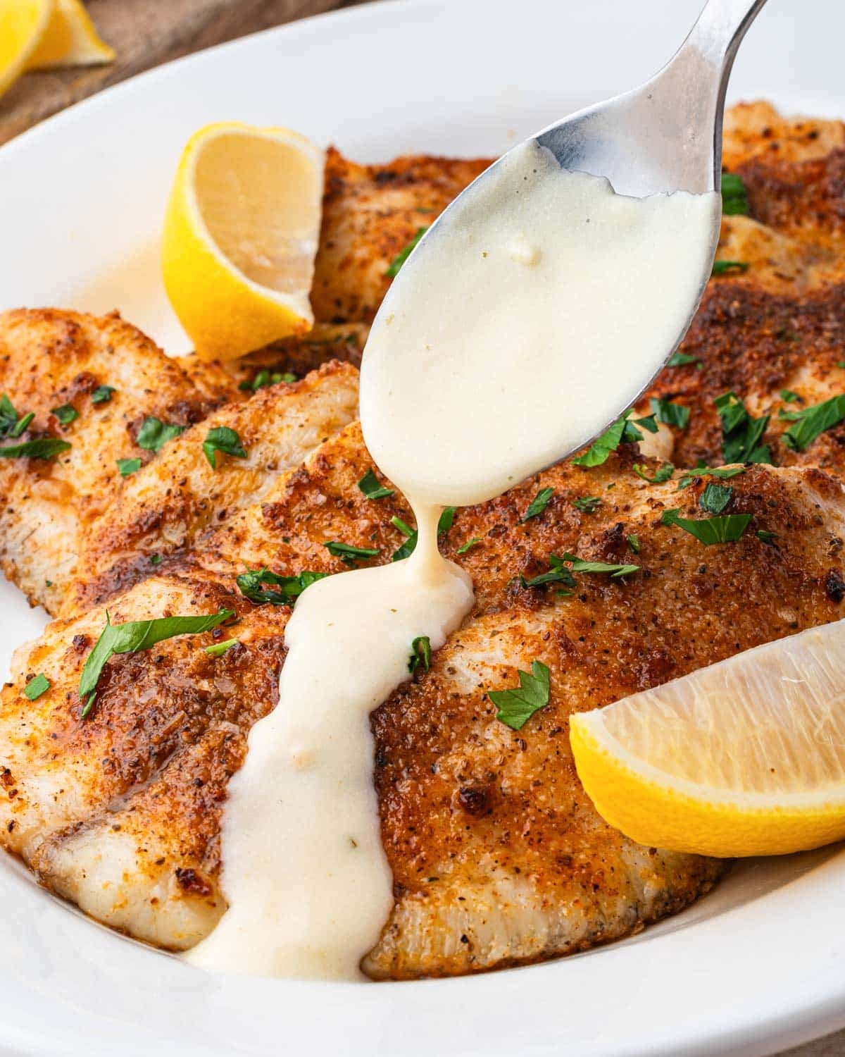 spooning lemon dijon sauce over tilapia