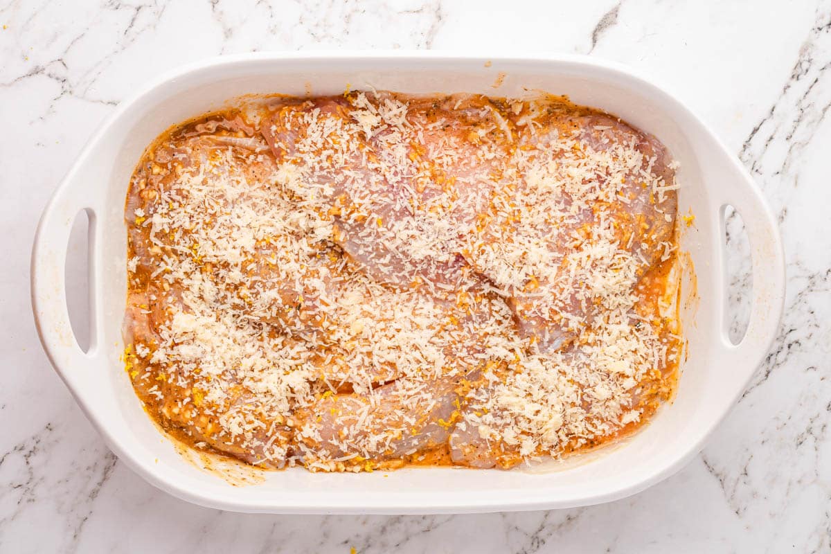 unbaked tilapia in a pan with cheese on top