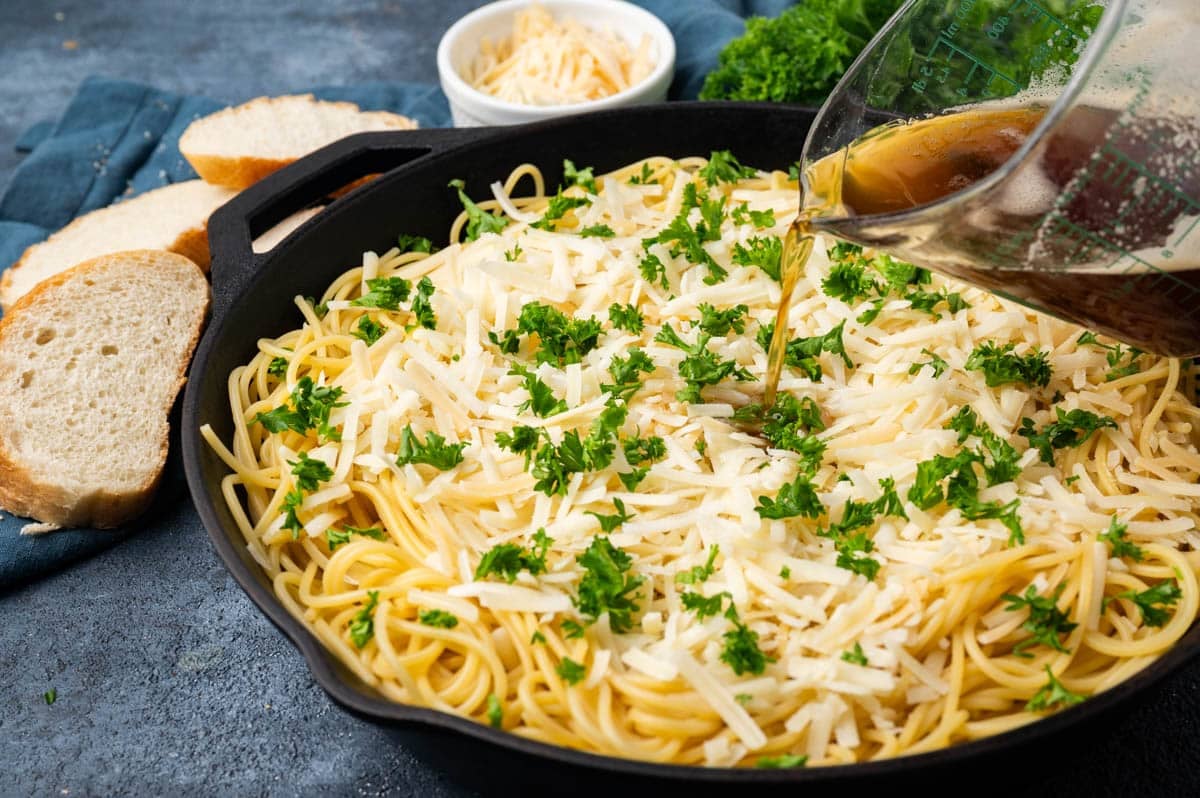 brown butter pouring over a skillet of spaghetti with cheese