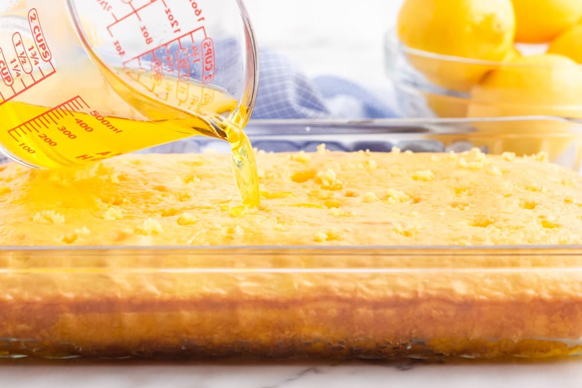 a cup pouring lemon jello over a baked cake