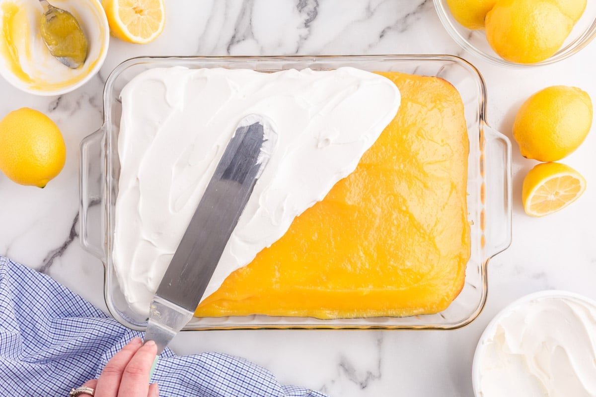 spreading cool whip over lemon curd on top of a baked cake