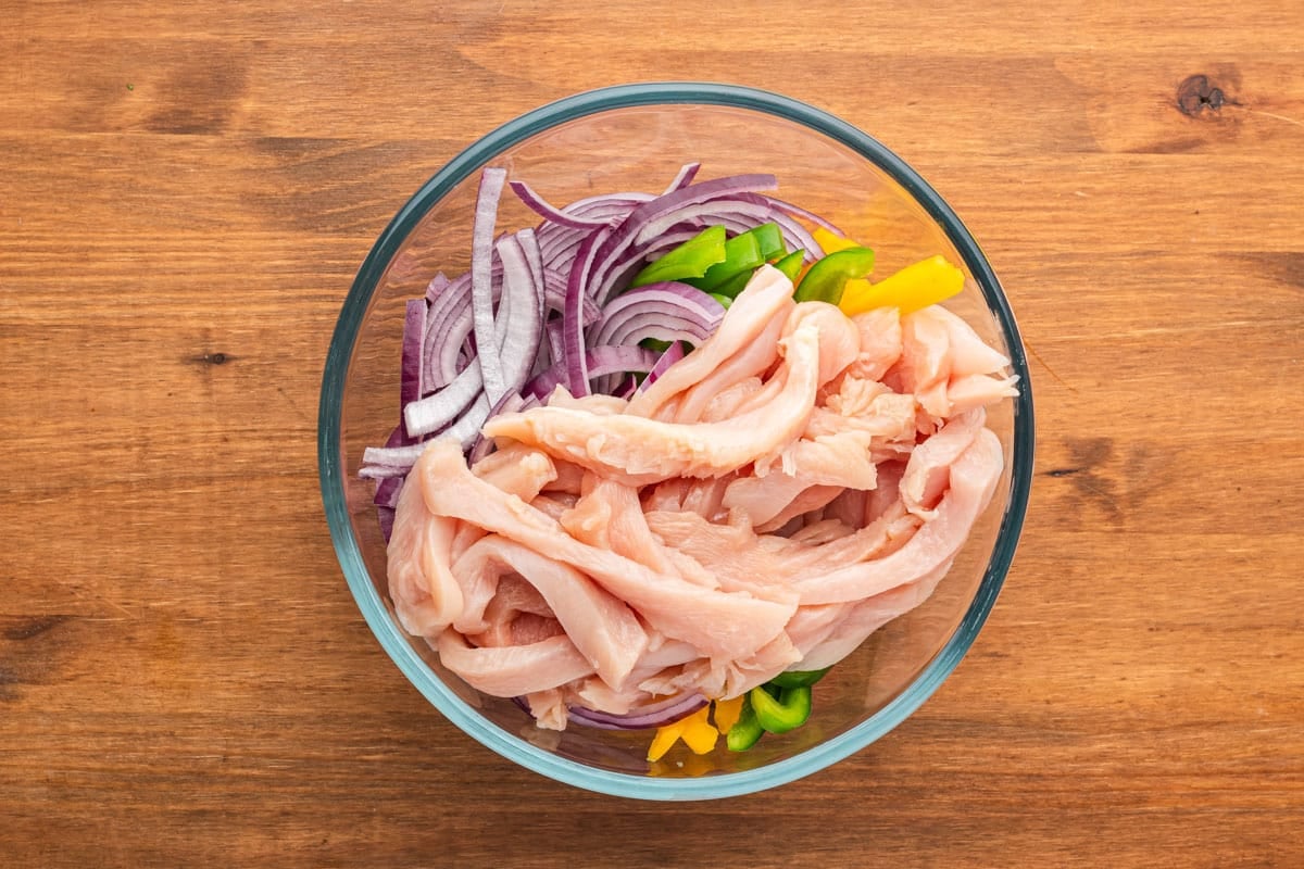 raw chicken, peppers and onions in a bowl