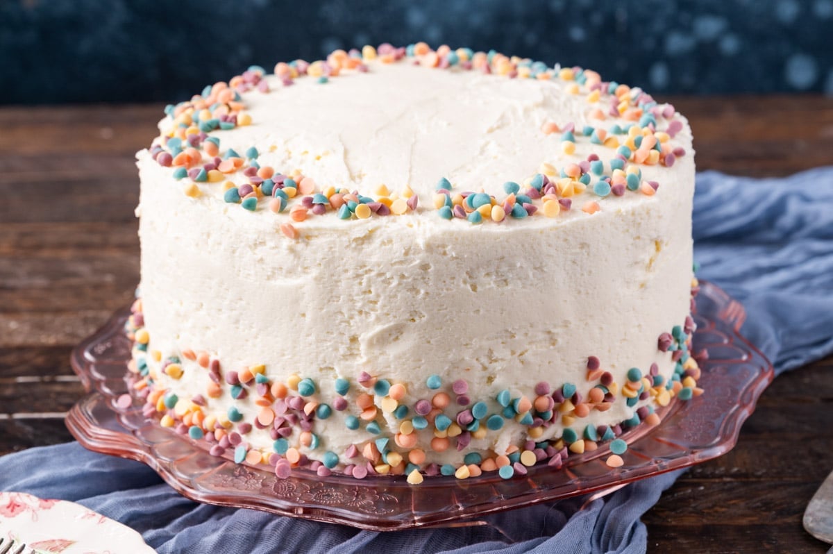 a layered cake with white frosting and rainbow chip sprinkles