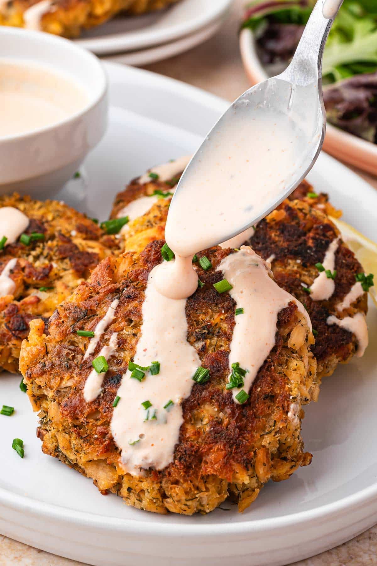 spooning spicy mayo over salmon patties on a plate