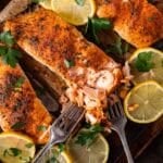 baked salmon on a baking sheet with forks flaking it apart