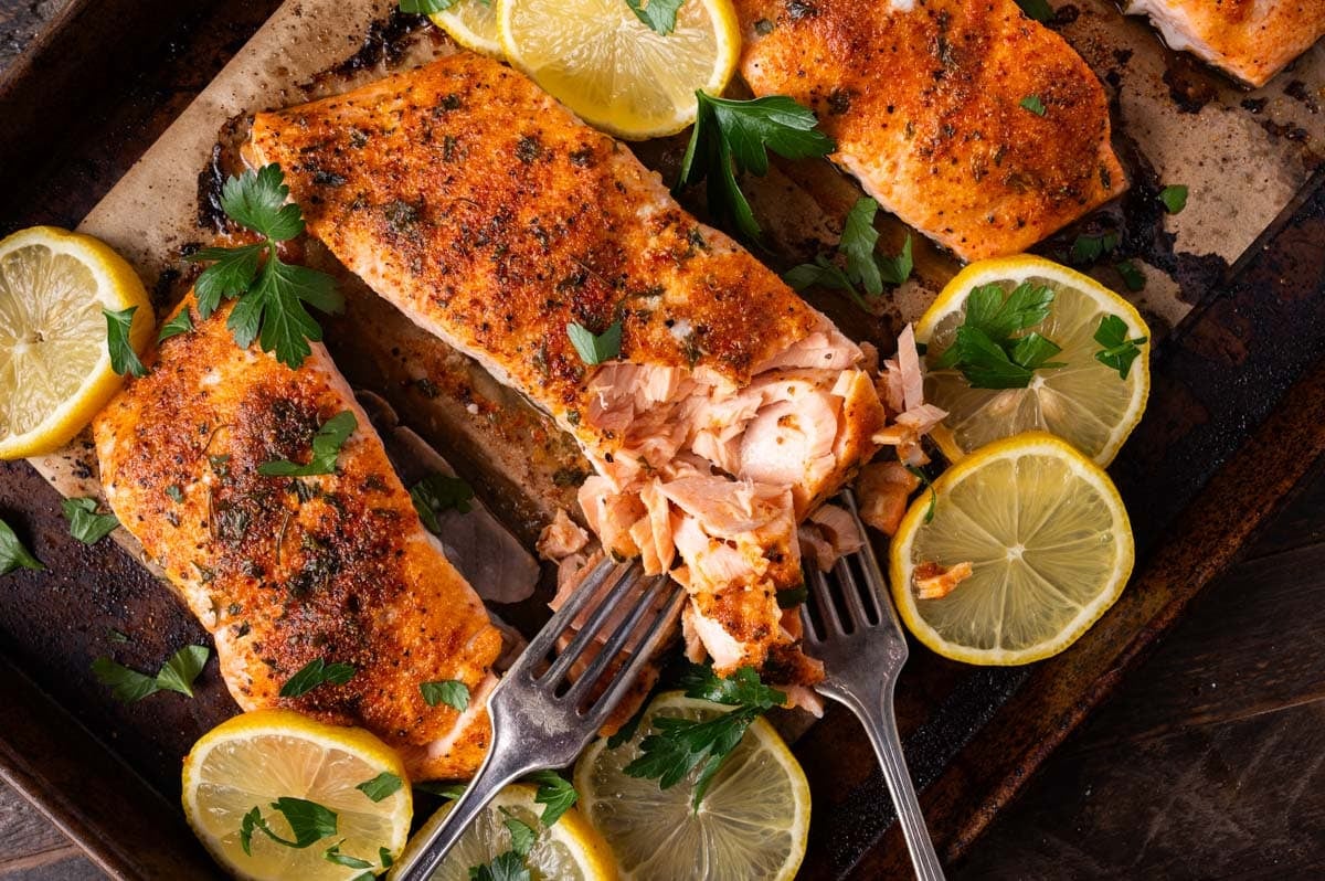 baked salmon on a baking sheet with forks flaking it apart