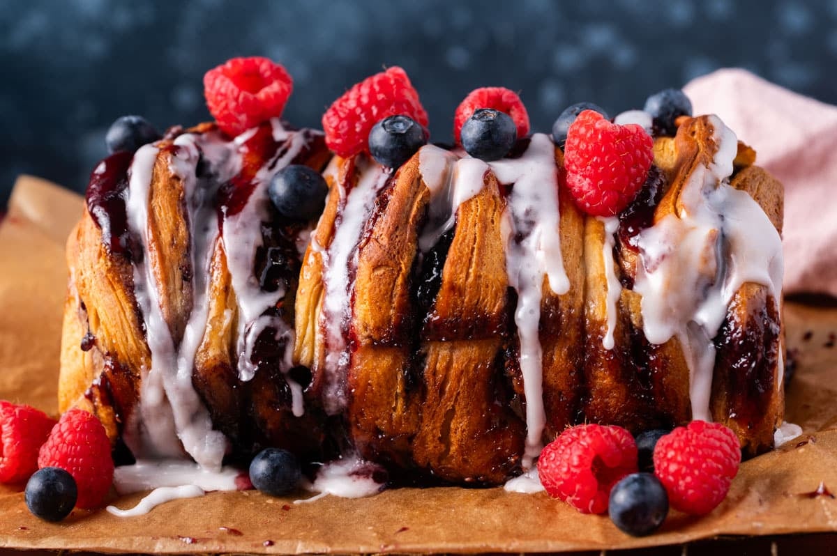 a loaf of berry pull apart bread with fresh berries and glaze