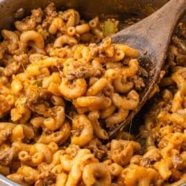a spoonful of elbow macaroni and cheesy hamburger in a skillet