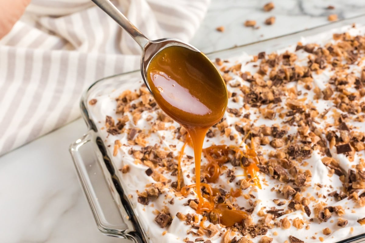 spoon drizzling caramel on top of a cake