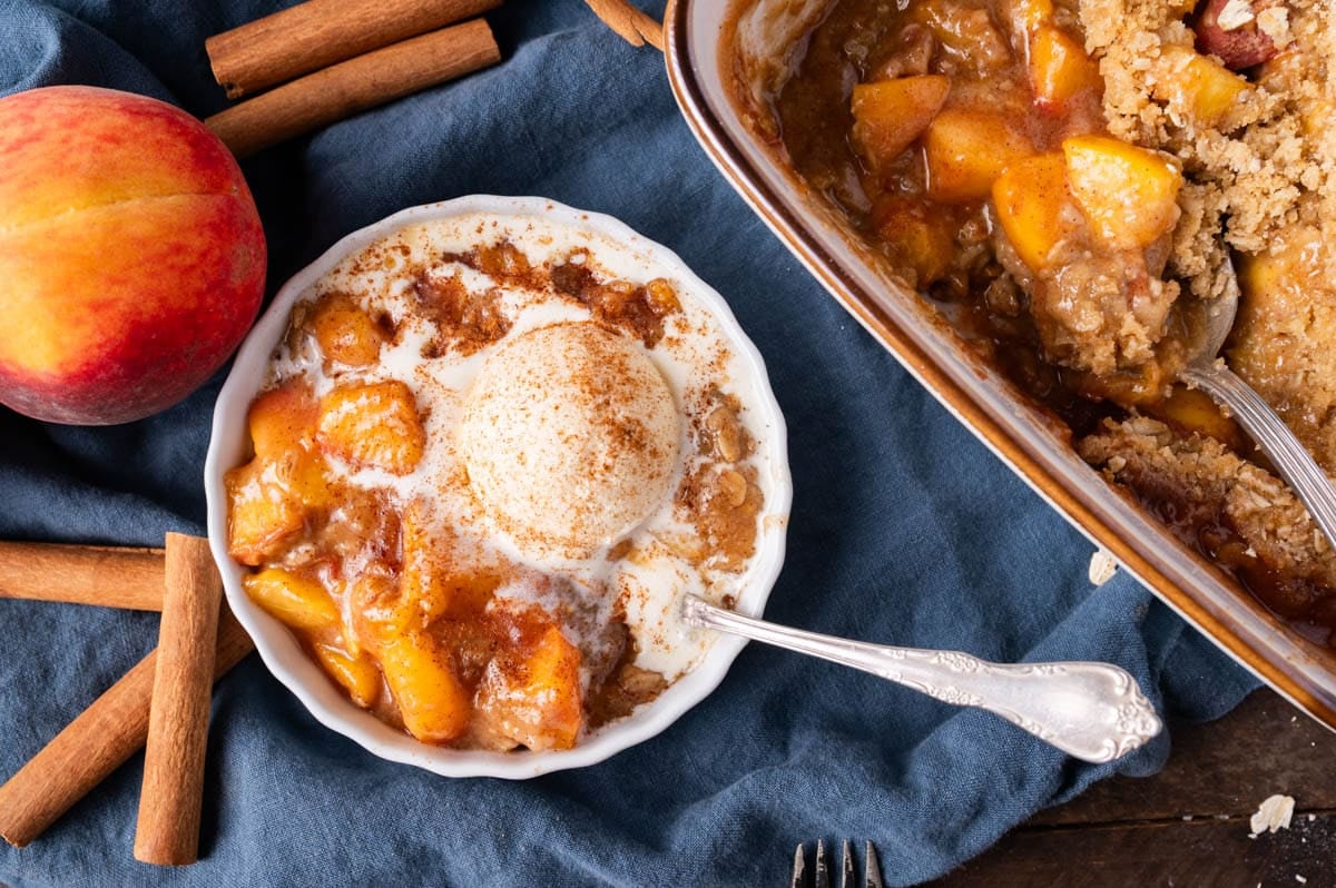 a bowl of peach crisp with ice cream on a table