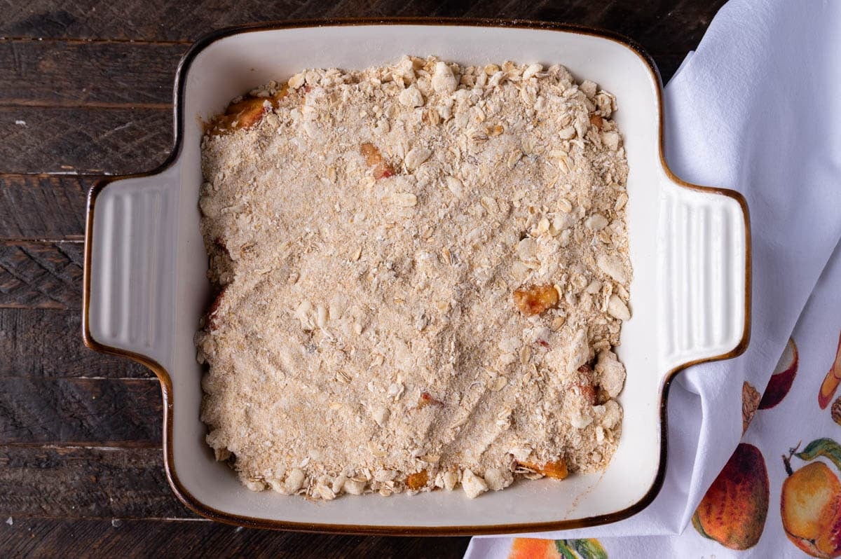 unbaked peach crisp in a white baking dish