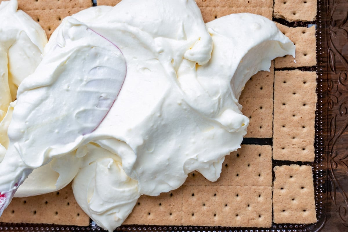 spreading whipped cream over graham crackers in a pan