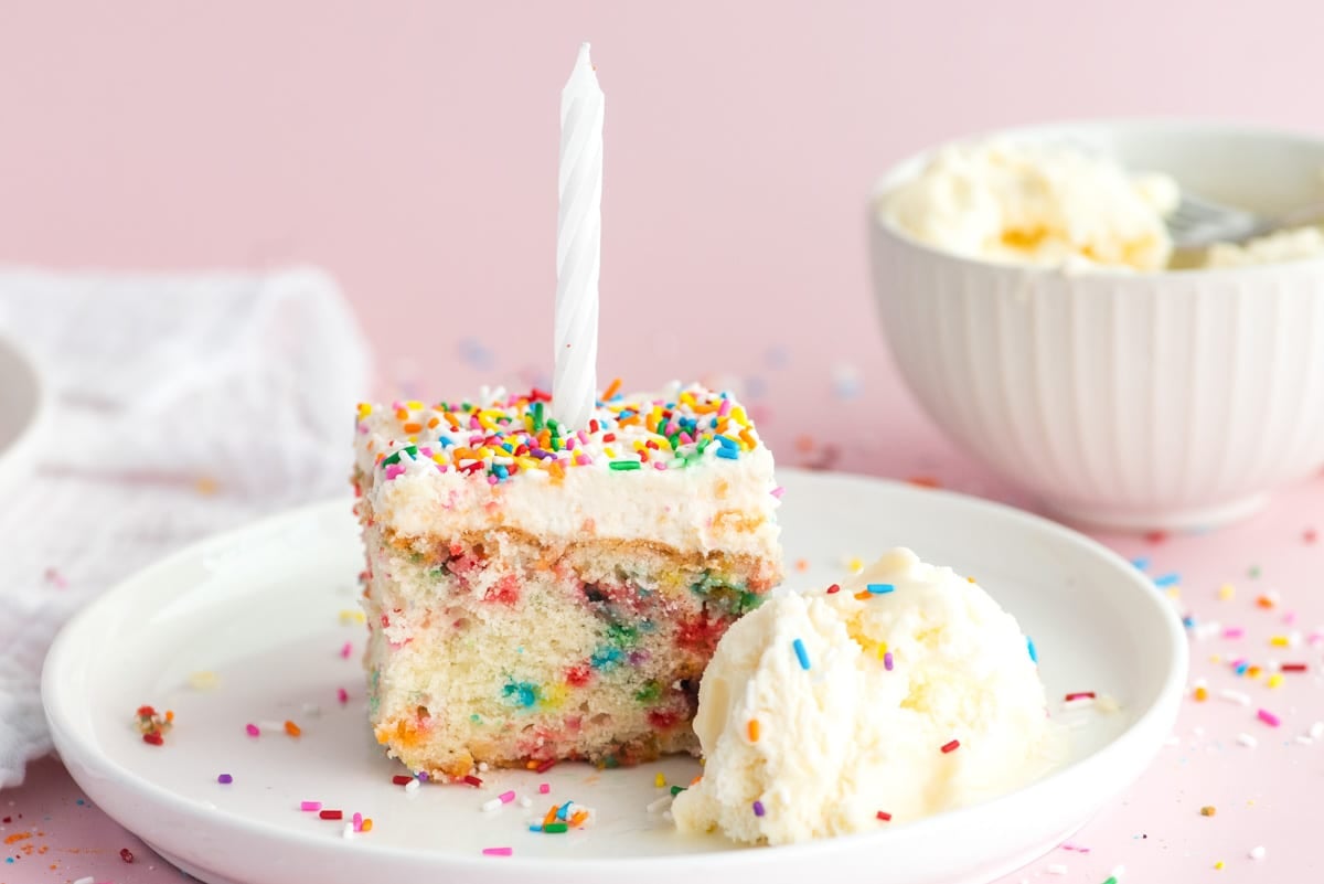 a piece of birthday cake on a plate with a candle and ice cream