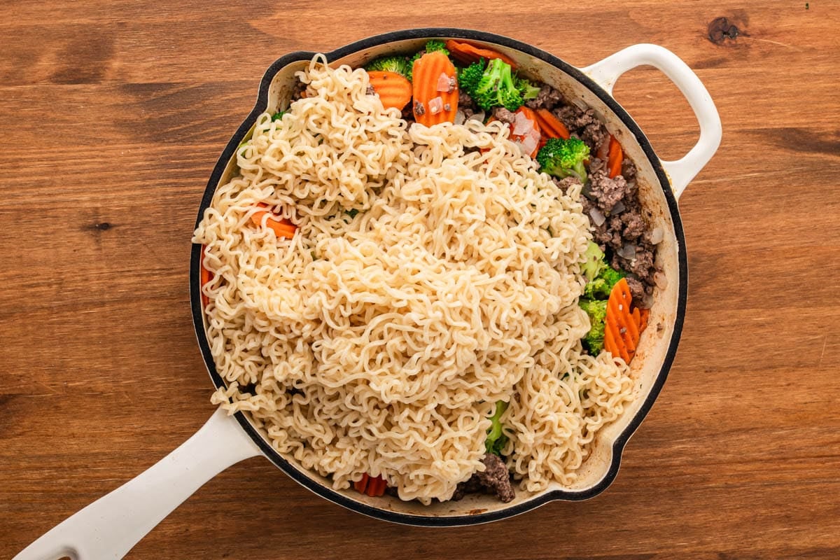 cooked ramen noodles over beef, carrots and broccoli in a skillet