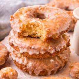 a stack of 3 old fashioned glazed donuts, one with a bite out