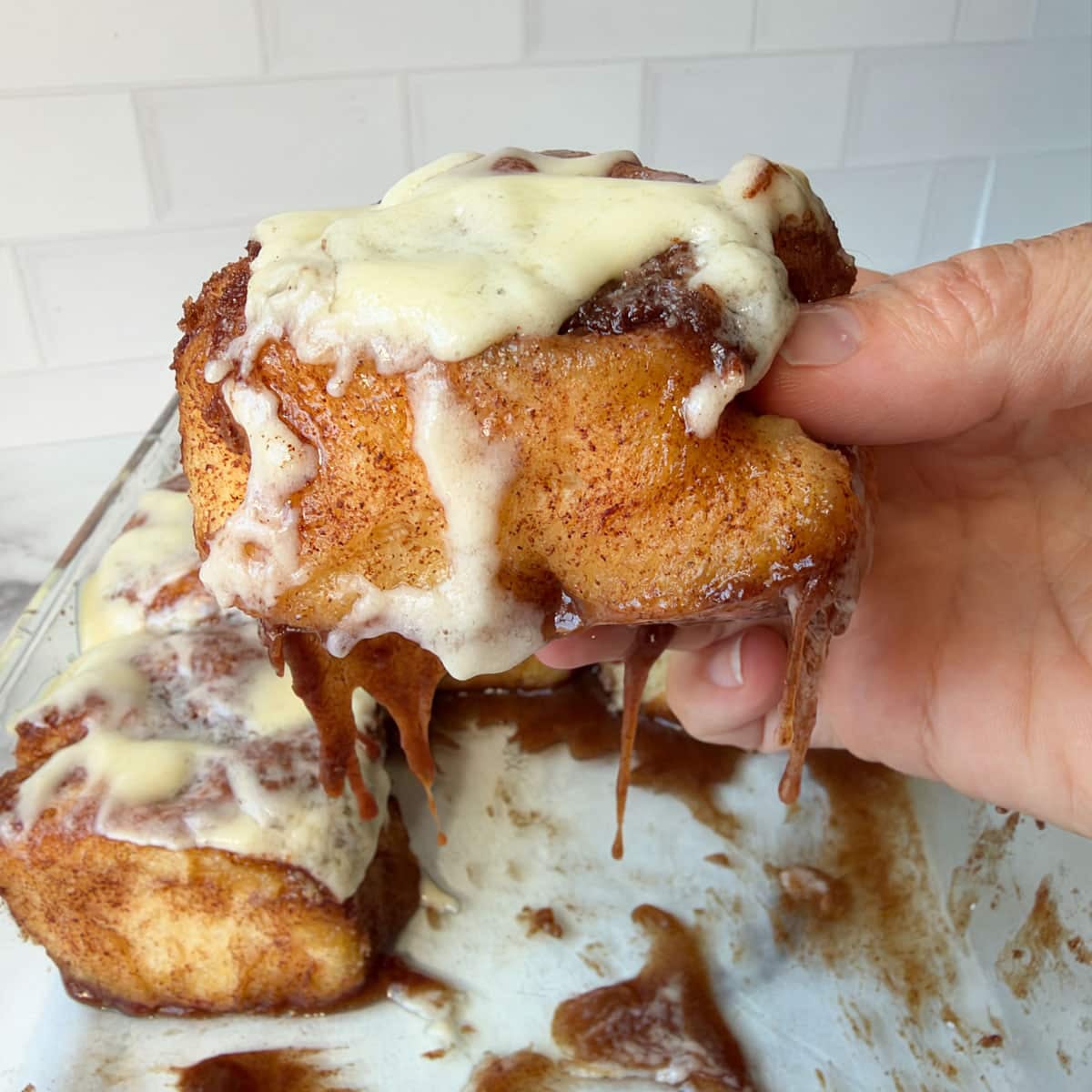 a hand holding a frosted cinnamon roll