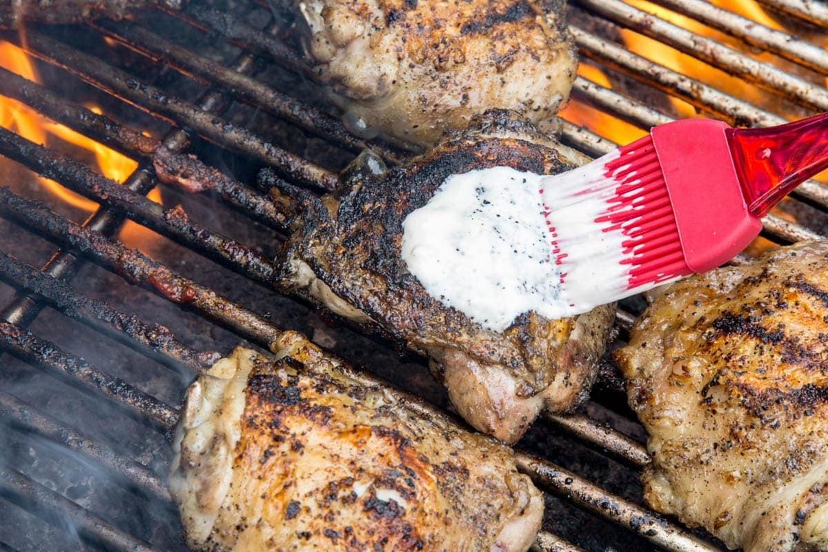chicken thighs on a grill with white bbq sauce