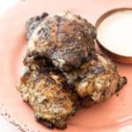 a pile of chicken thighs on a plate with white bbq sauce