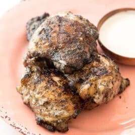a pile of chicken thighs on a plate with white bbq sauce